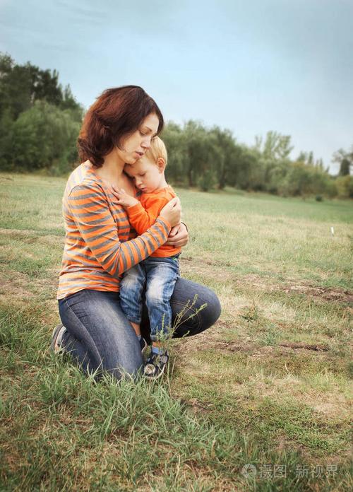 他的小儿子和妈妈拥抱绿色的林间空地的背景